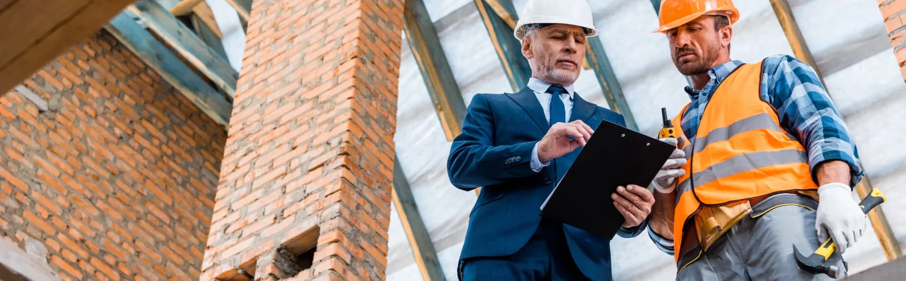 A business owner in a suit reviewing a checklist with a construction worker on site.