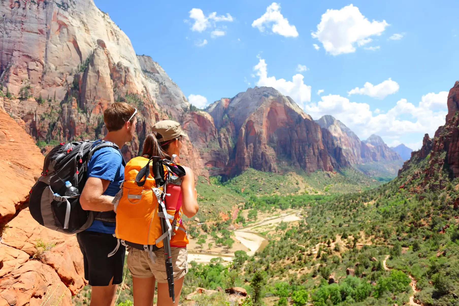 Two hikers with backpacks pausing on a ridge to look out over a canyon valley.