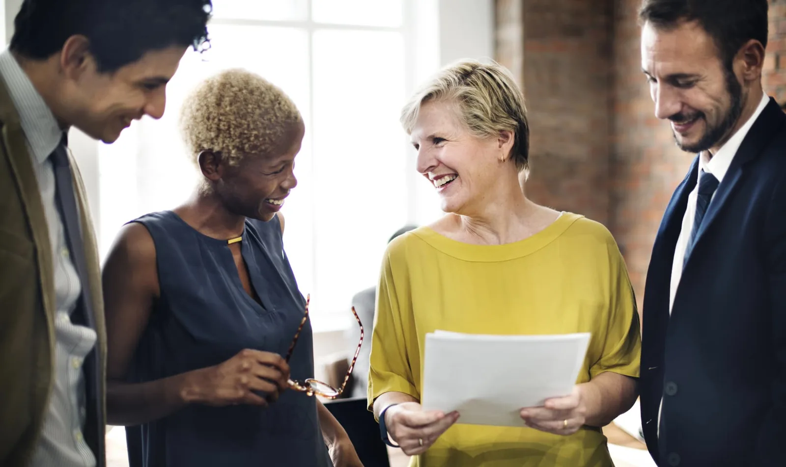 Four colleagues of different ages smiling as they review a document together in an office.