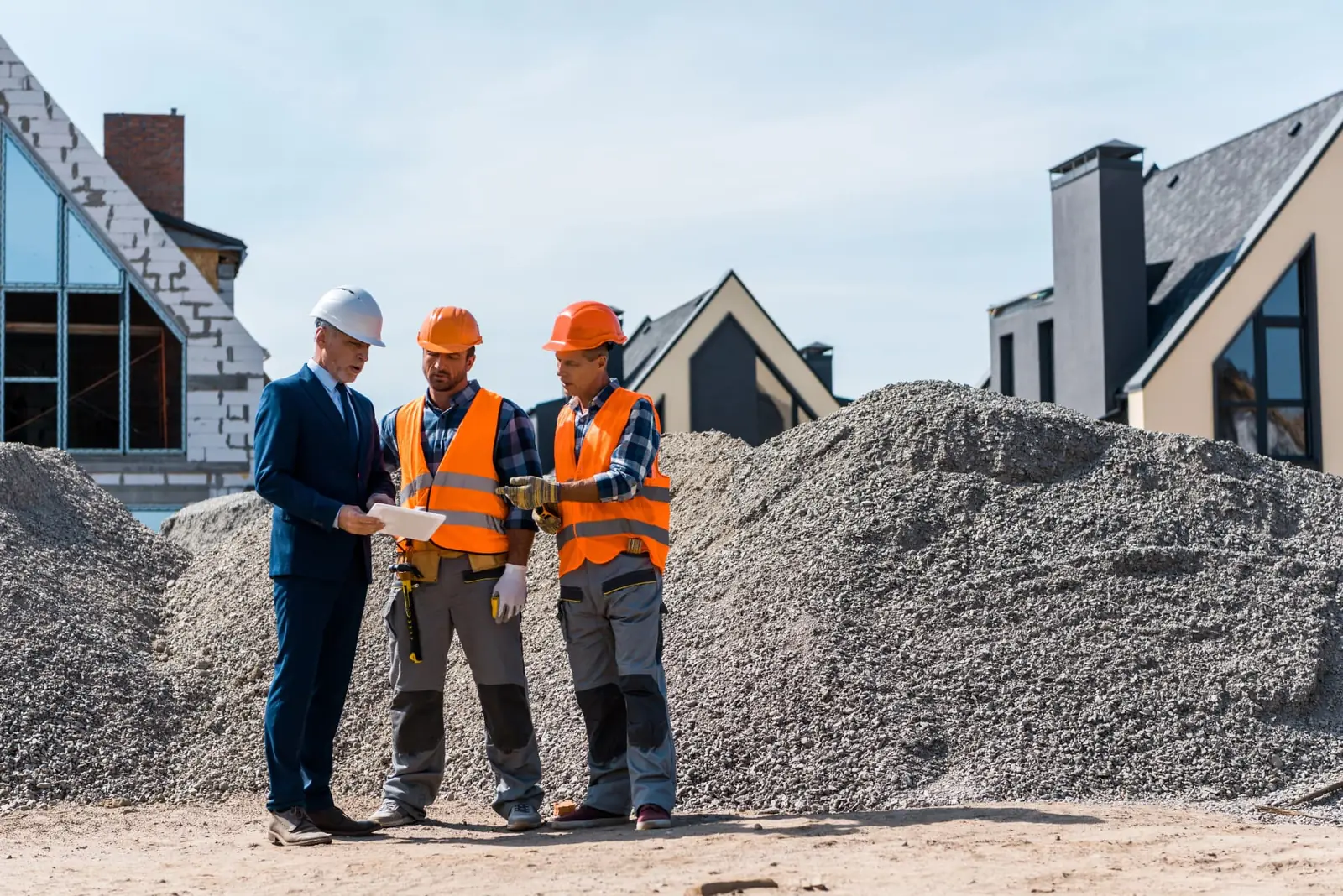 A business owner in a suit reviewing plans with two construction workers at a housing development.